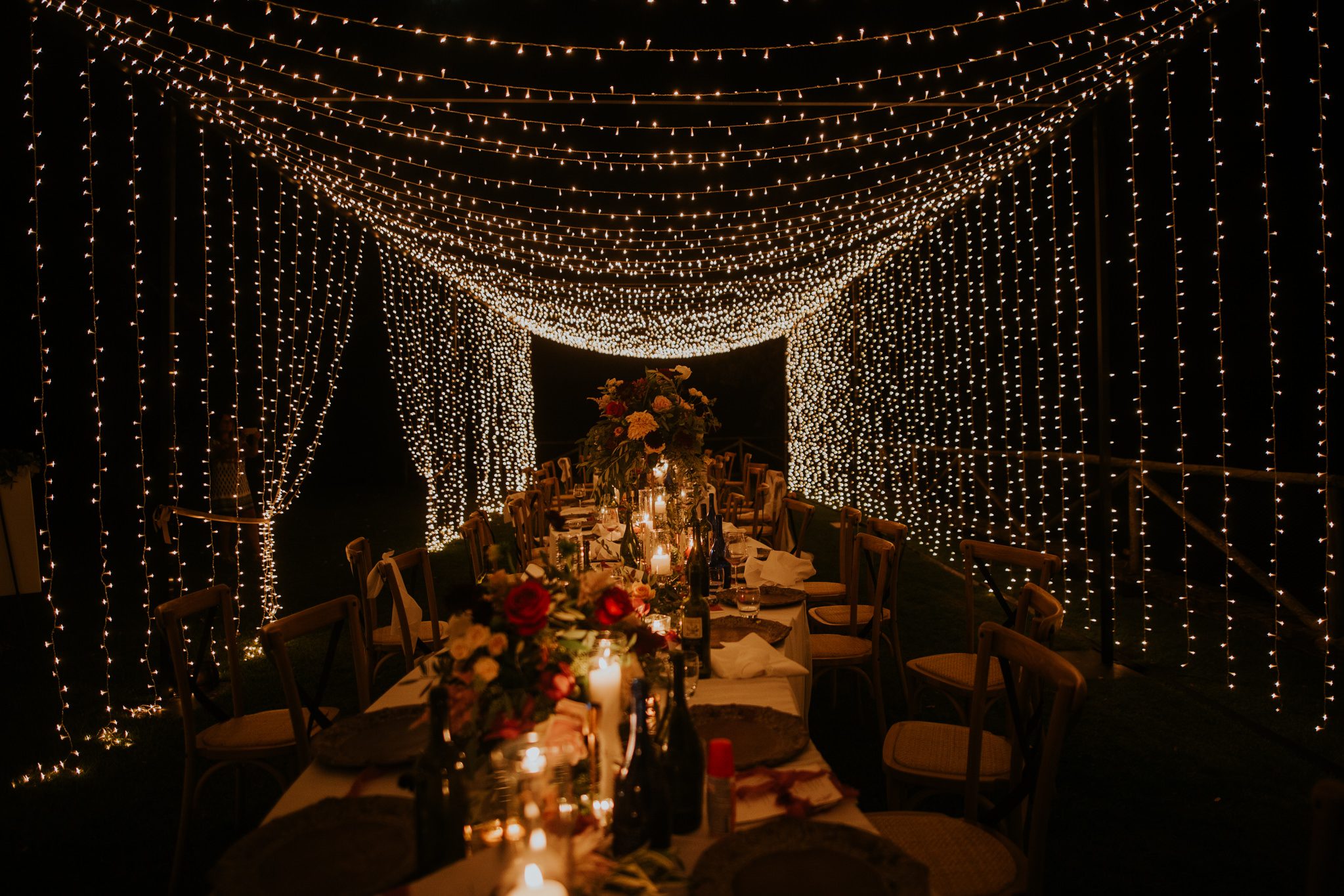 A long tabe with shimmering lights, flowers and fruit, set up of a wedding dinner in Siena Tuscany Italy