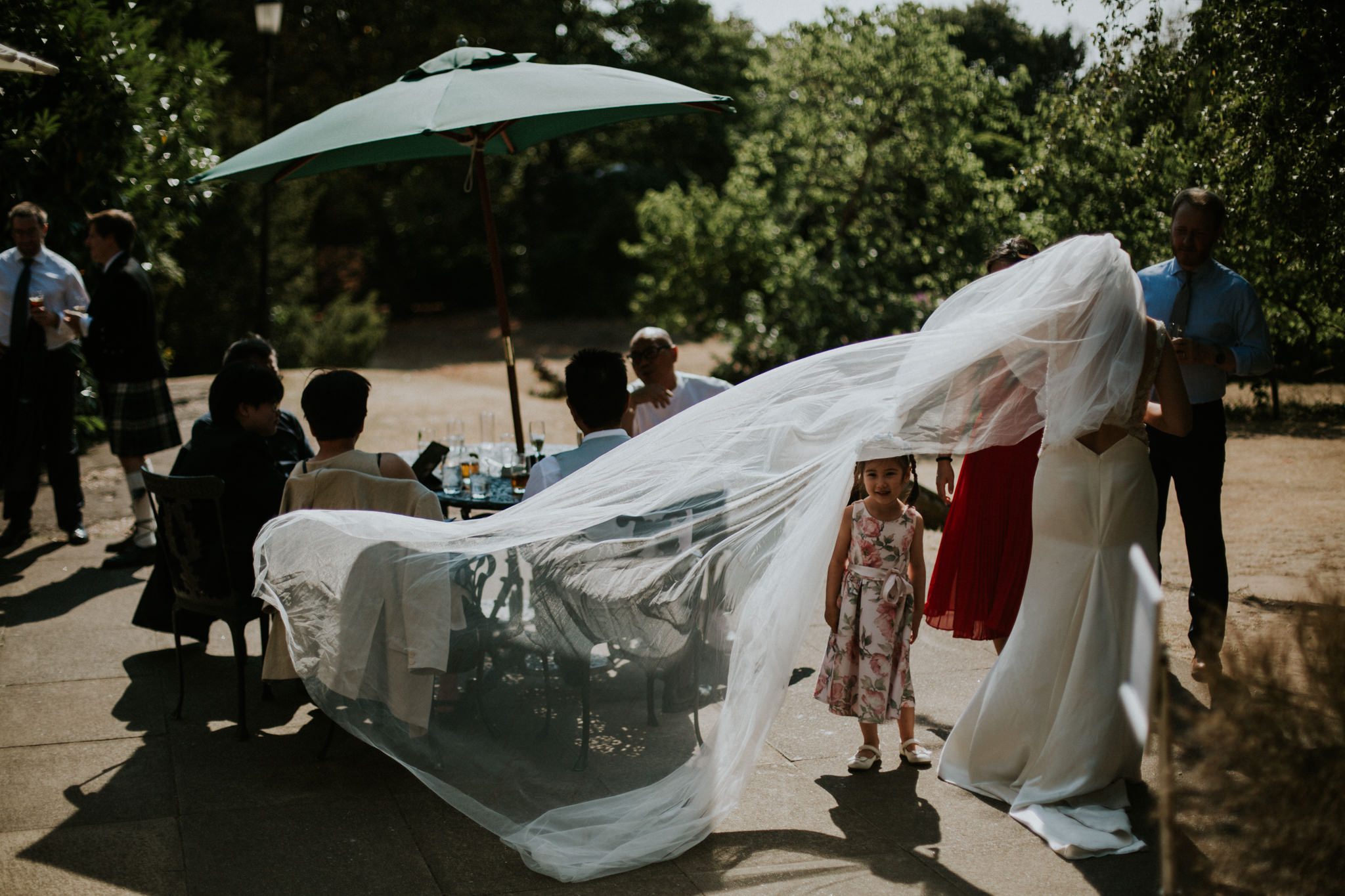 A small girl peeps out from underneath the bride's veil as it is caught by the wind