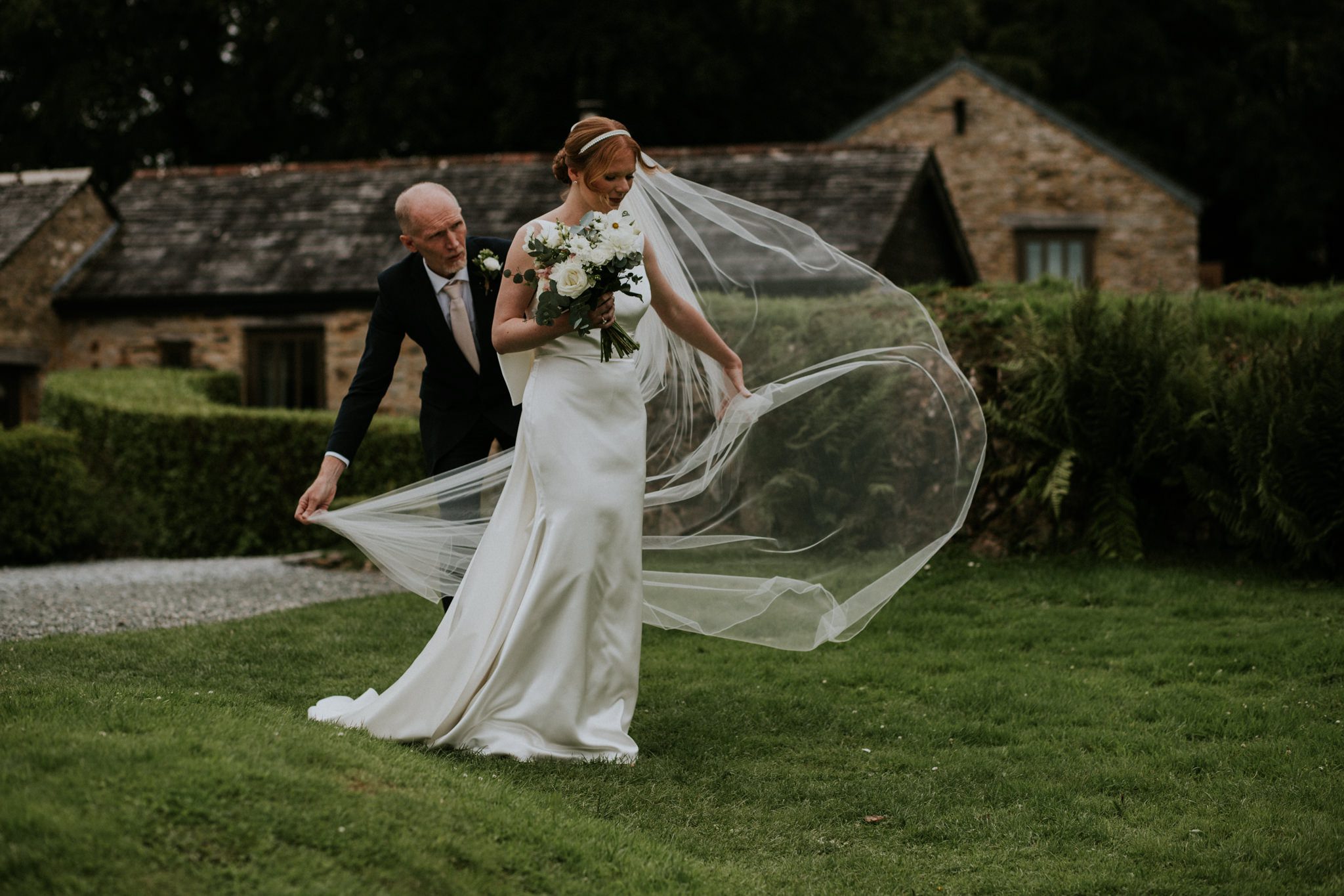 The brides father adjusts her veil in the wind at a wedding ceremony at Trevenna Barns in Cornwall