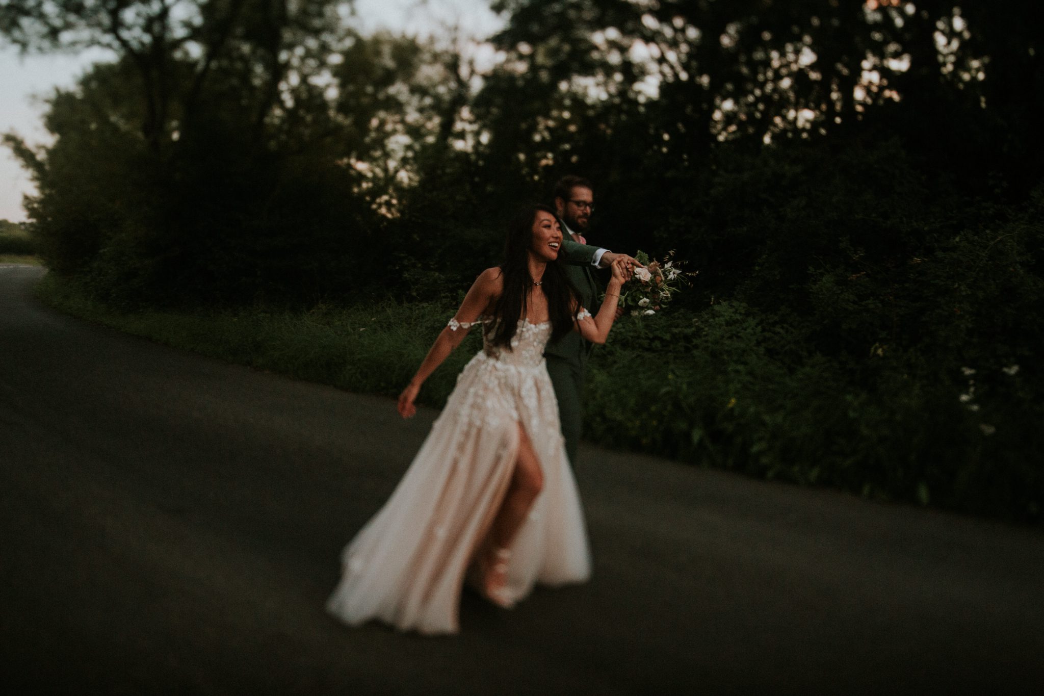 The bride and groom run down a road laughing after their wedding at Upthorne Wood in Suffolk