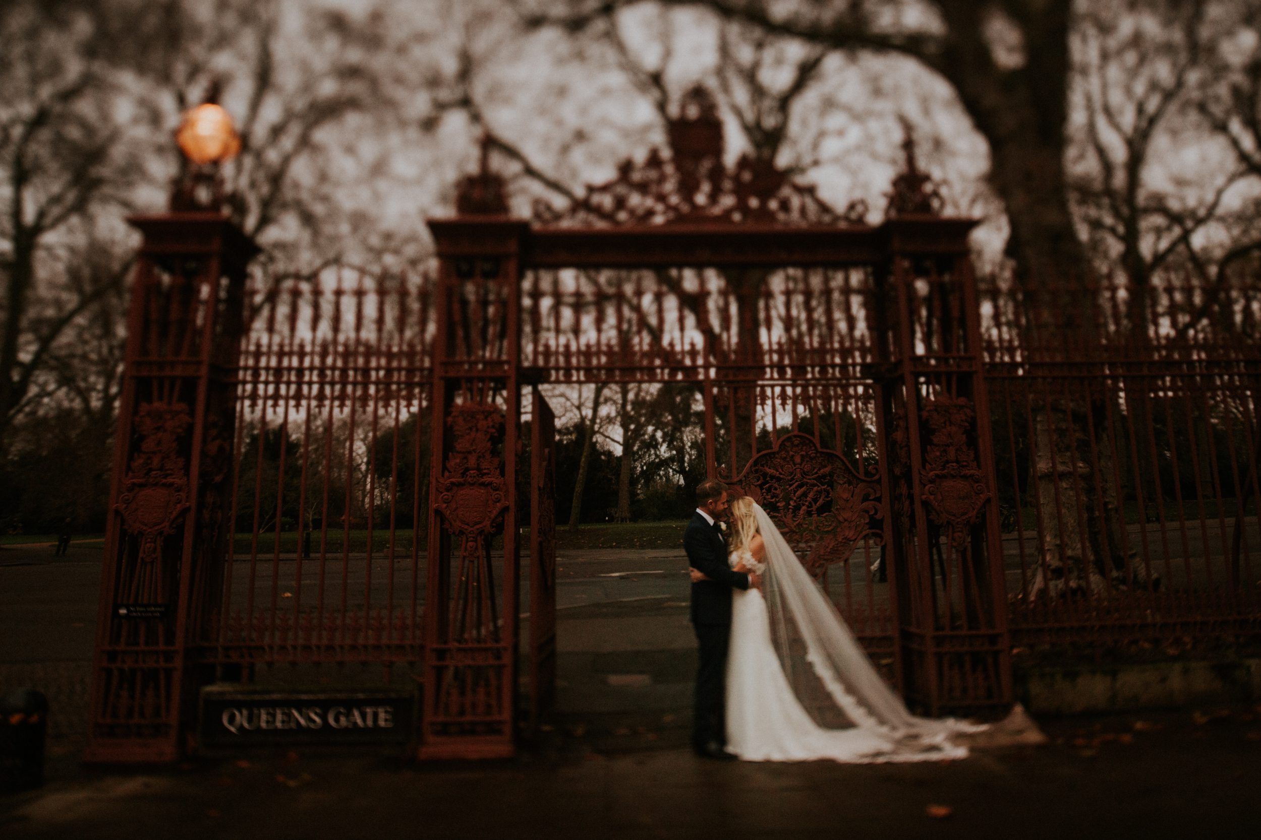 A bridal portrait of a bride and groom kissing in front of Elizabeth Gate in London