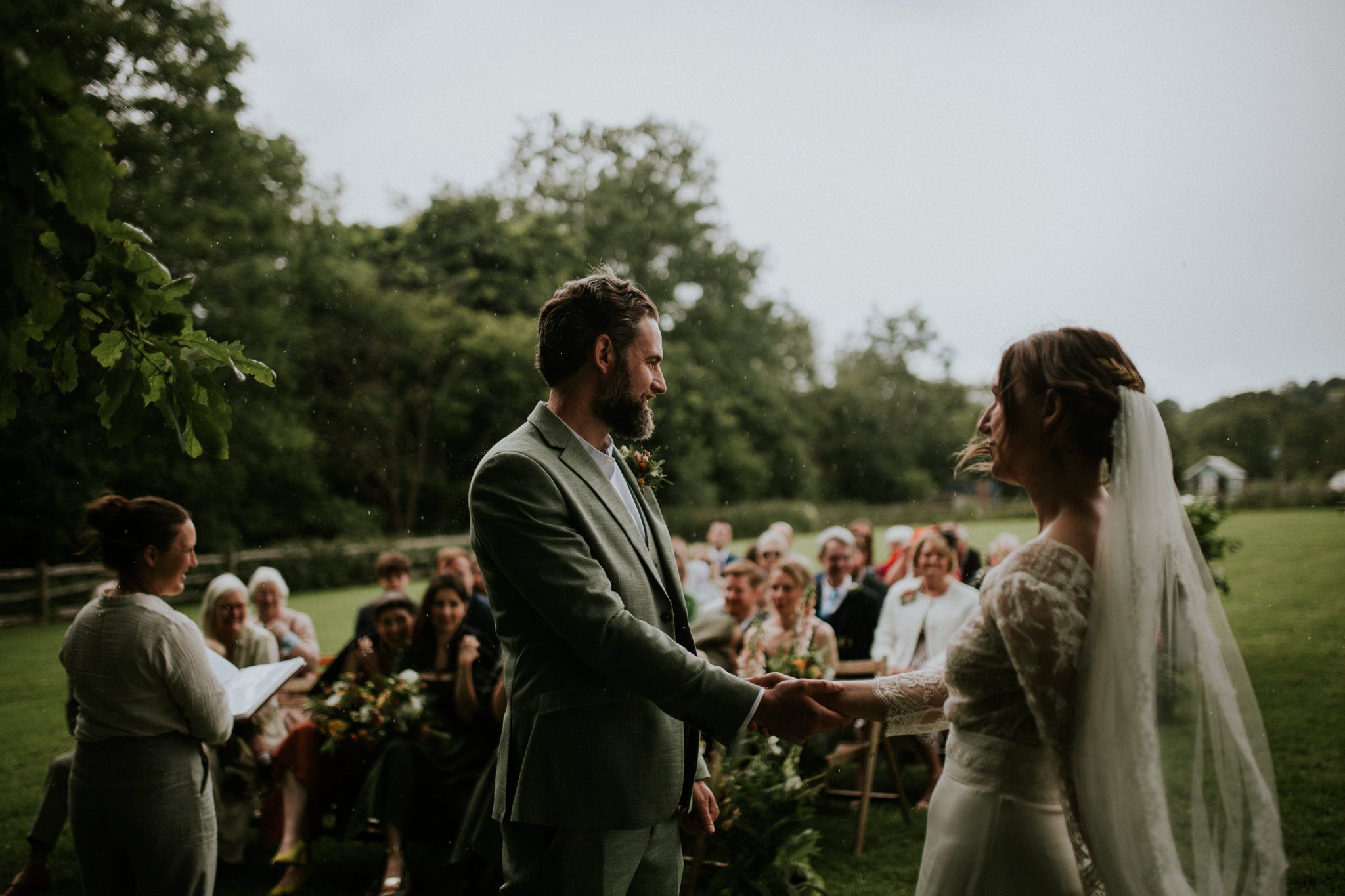 A bride and groom hold hand in front of their guests at their Wild Wedding at Lower House Farm in Herefordshire