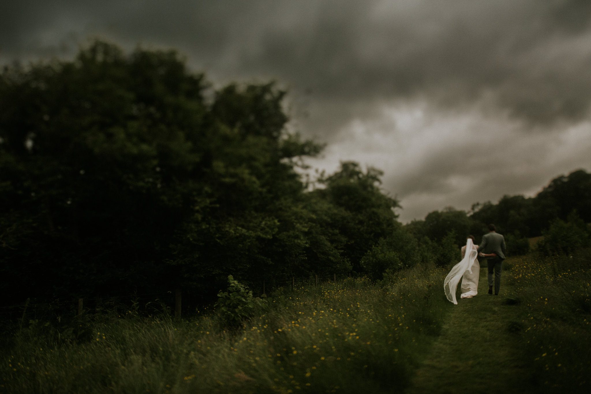 A bride and groom walk under stormy skies after their wedding at Lower House Farm in Herefordshire