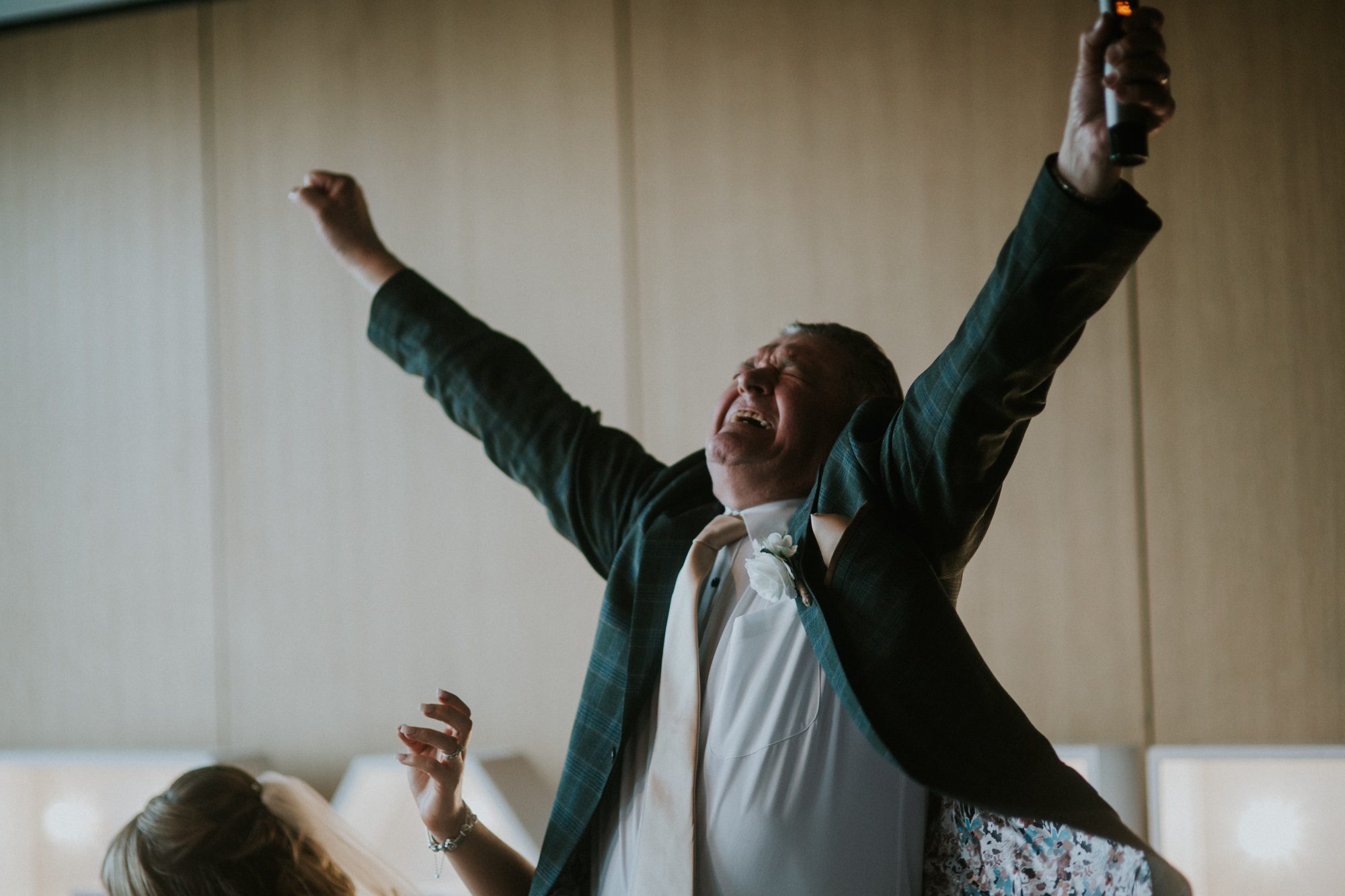 A happy father of the bride throws his arms in the air in celebration at the wedding of his daughter at Above the Bay in Falmouth