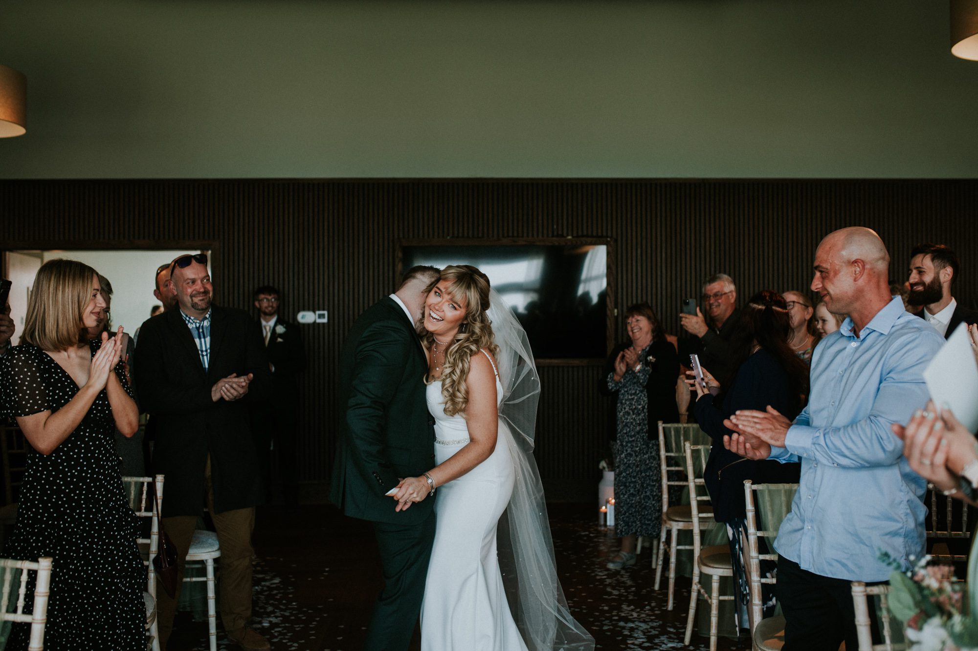 A bride and groom laughingly share a kiss as they leave their wedding ceremony at Above the Bay in Falmouth