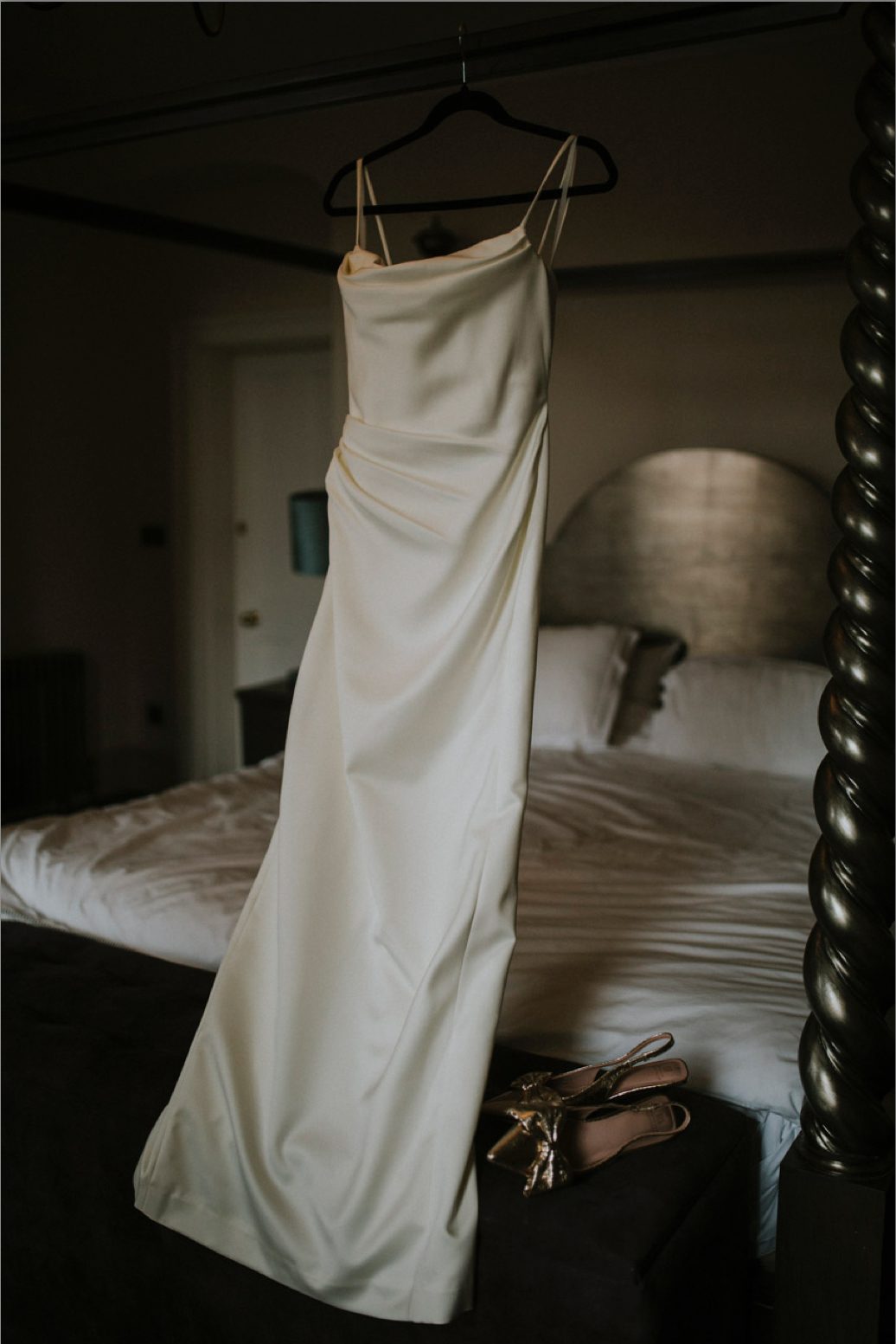 A detail shot of a wedding dress hanging from a four poster bed