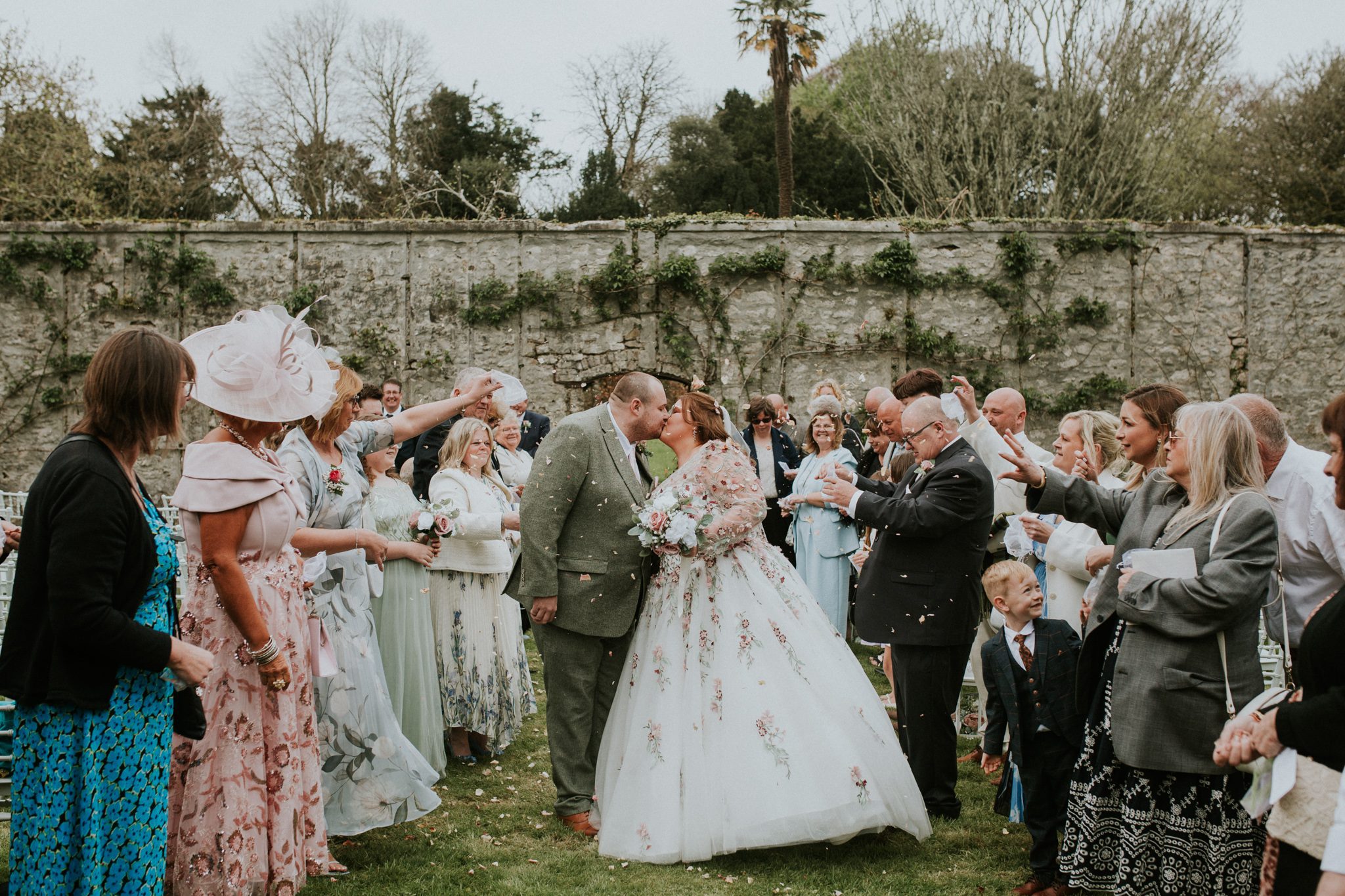 A newly married couple share a kiss under a shower of confetti at their wedding at Scorrier House in Cornwall