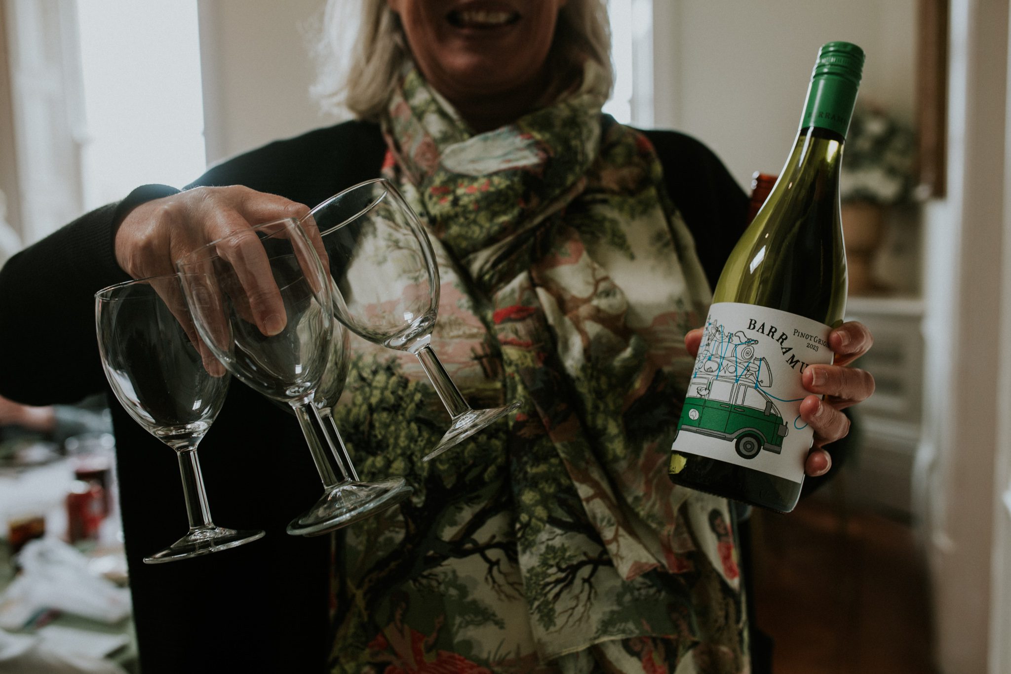 A wedding guest brandishes a bottle of wine and three glasses at Scorrier House in Cornwall