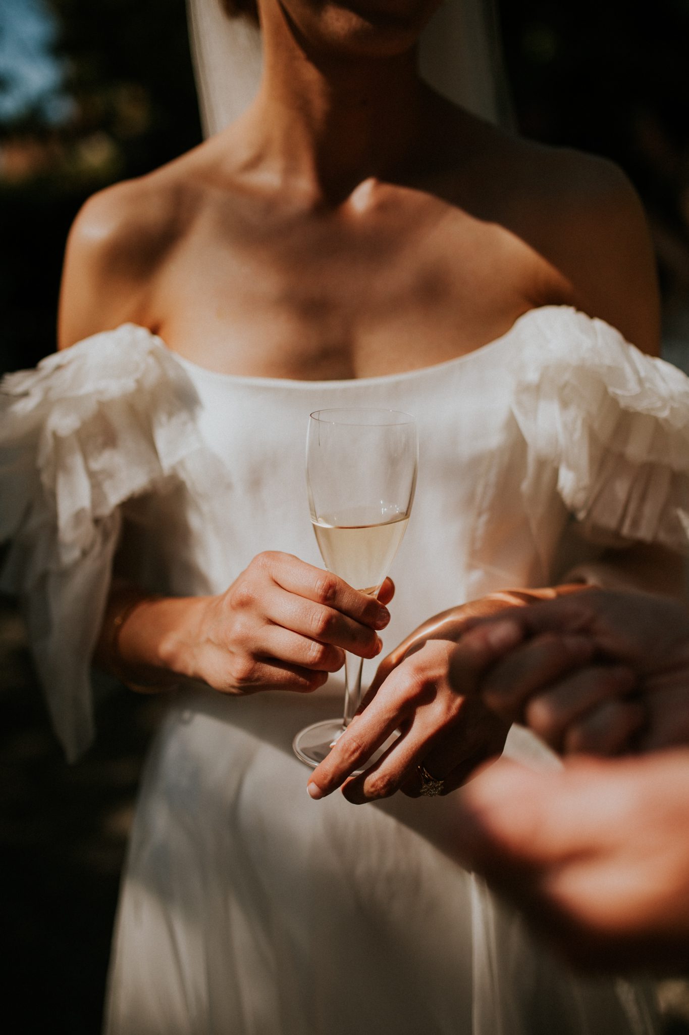 A bride wearing Kate Halfpenny holds a flute of champagne during her wedding reception after her wedding at The Lost Music Hall at Great Ambrook in Devon