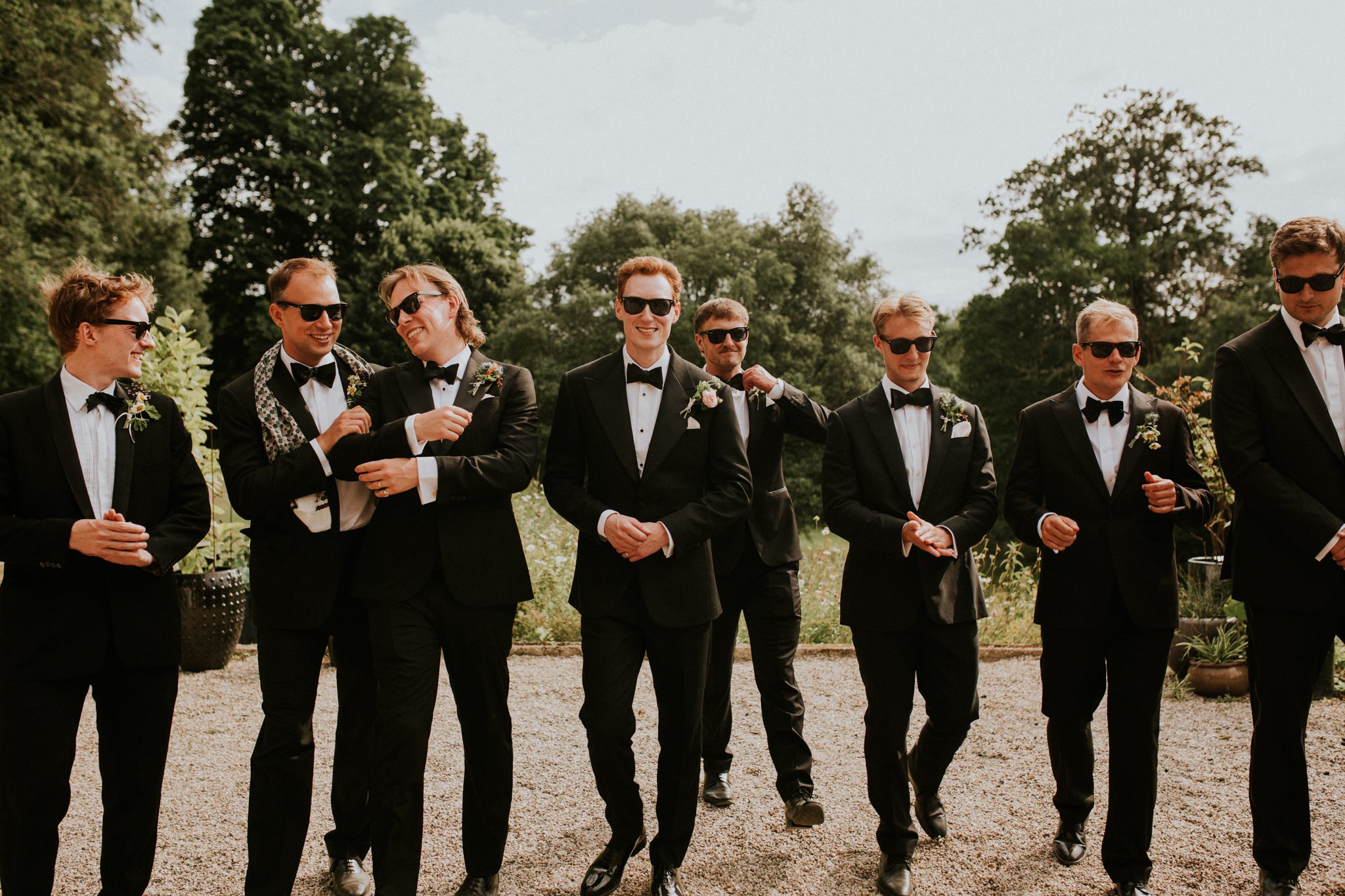 Ushers in black time walk and talk with the groom in an editorial image during a wedding at The Lost Music Hall at Great Ambrook in Devon