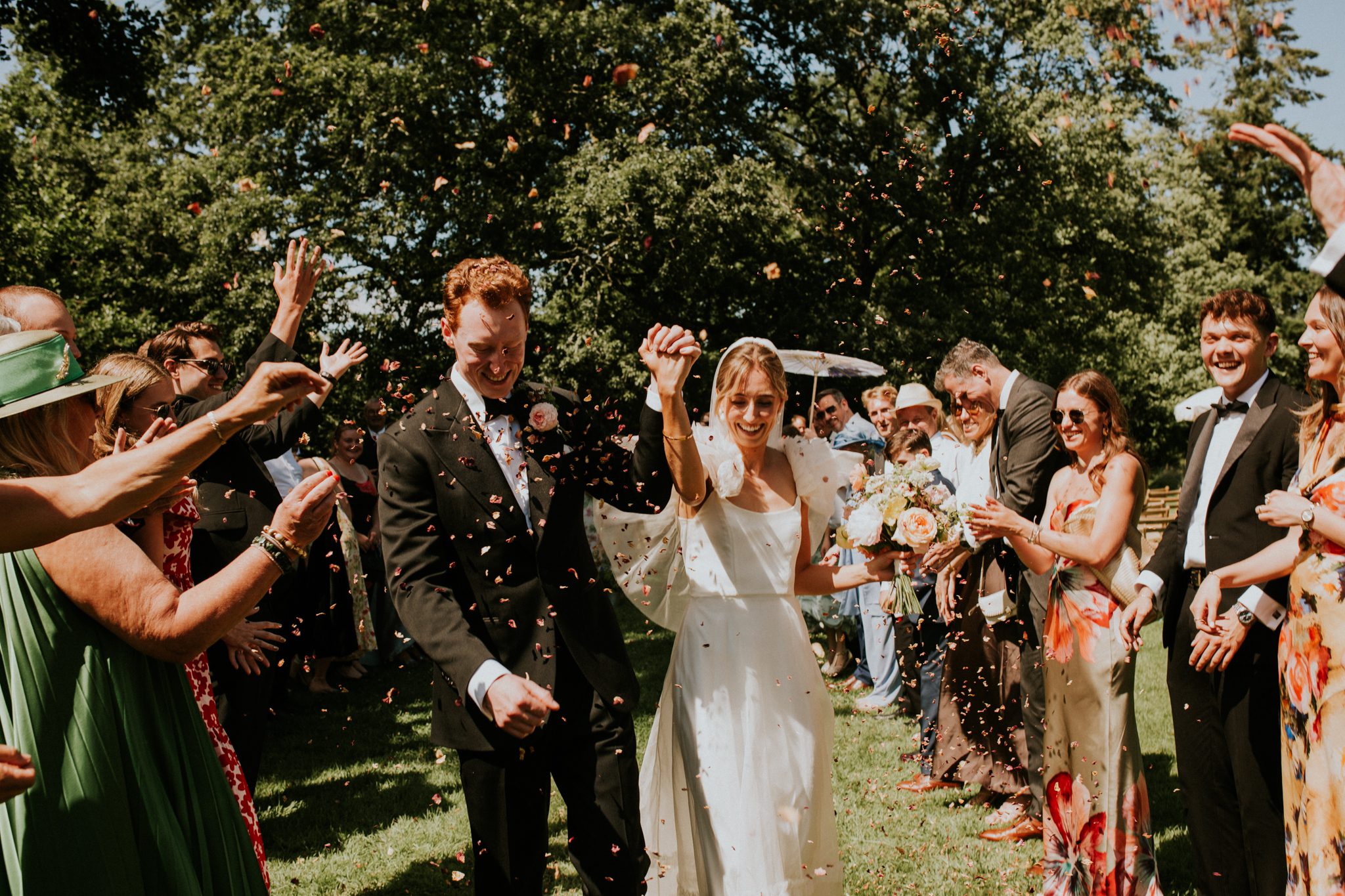 A happy bride and groom walk under a shower of confetti after their wedding ceremony at The Lost Music Hall at Great Ambrook in Devon